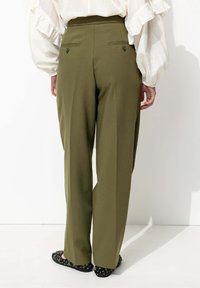Pantalons taille haute vert olive avec une coupe droite, dotés de deux poches arrière et d'une texture de tissu lisse. Ballerines noires à motifs.
