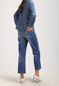 Jeansskjorta med långa ärmar och knappade manschetter, matchad med ljusblå vida jeans. Vita sneakers kompletterar outfiten.