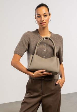 Light gray leather handbag with a smooth texture, curved design, and a single top handle. Features gold embossed brand logo.