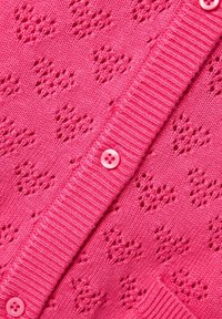 Rozā adīta kardigāna ar teksturētu mazu sirsniņu rakstu, ar ribota apkakli un vienu rozā pogu aizdarīšanai.