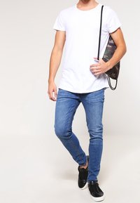 Camiseta blanca de manga corta, jeans ajustados de color azul, zapatillas negras y una mochila de cuerda de camuflaje. Diseño de atuendo simple y casual.