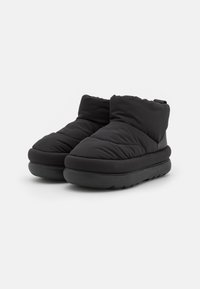 Botas de tobillo impermeables negras con un diseño acolchado, textura suave y una suela gruesa y acolchada. Presenta una silueta minimalista.