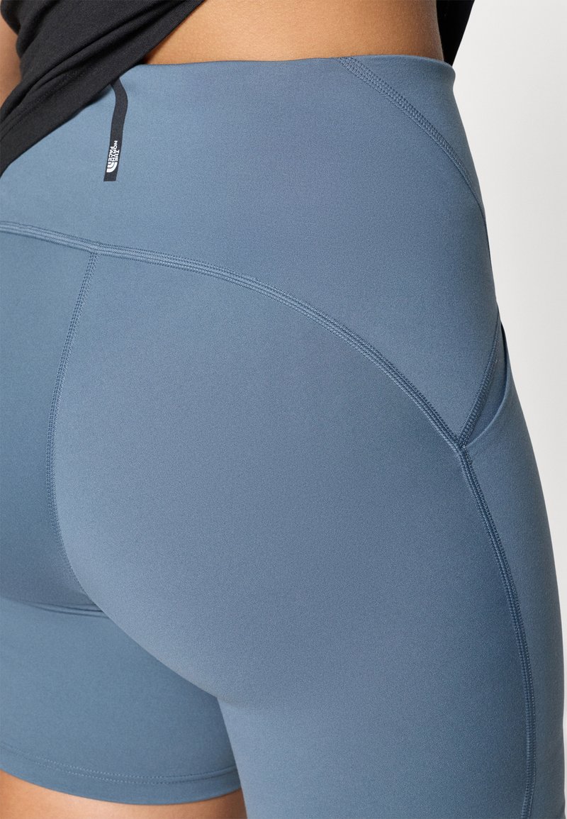 Pantaloni sportivi azzurri chiari con una texture liscia e elasticizzata. Presentano cuciture curve e un'etichetta nera vicino alla vita.