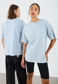Lyseblå oversized t-skjorter i bomull; avslappet passform med senket skuldre, kombinert med svarte shorts. Minimalistisk design uten mønstre.