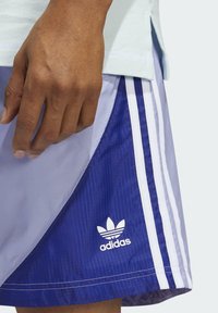 Pantaloni corti Adidas realizzati in materiale blu e viola con strisce bianche. Presentano un logo in basso a sinistra e dettagli in tessuto testurizzato.