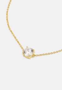 El collar de cadena de oro presenta una gema redonda y transparente colocada en un engaste de seis garras en el centro, mostrando una superficie pulida y un diseño delicado.