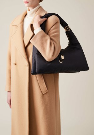 Black padded handbag with a curved strap and gold hardware detail, held by a person in a beige coat against a neutral background.