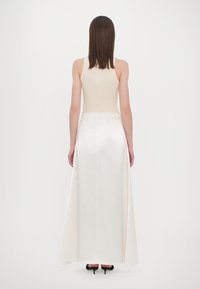 Sleeveless cream top paired with a long, flowing white skirt made of a textured fabric, featuring a waistband and split hem. Black heels.