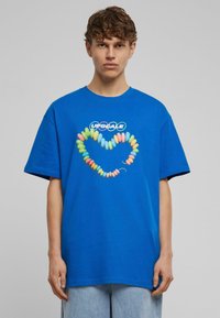 Blå bomulds T-shirt med et farverigt slikhalssmykke grafik, med teksten "UPSCALE" ovenfor. Korte ærmer og rund halsudskæring.