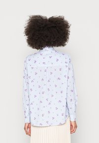 Lys blå skjorte med lodrette hvide striber, prydet med små lilla blomster mønstre. Har lange ærmer og knapmanchetter.