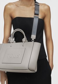 Sac fourre-tout synthétique gris avec une surface texturée, doté de poignées nouées et d'une bandoulière amovible embossée avec "TOUS".