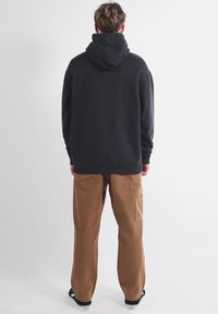 Sweat-shirt à capuche noir associé à un pantalon utilitaire beige. Le sweat-shirt a une coupe décontractée et des poignets côtelés ; le pantalon est doté de poches latérales et d'une jambe droite.