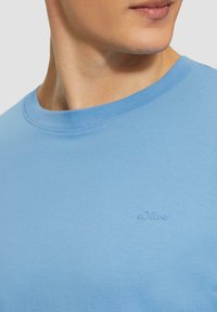 Jasnoniebieska koszulka wykonana z bawełny, z okrągłym dekoltem. Posiada subtelnie wyszyte logo s.Oliver na górnej części klatki piersiowej. Gładka tekstura.