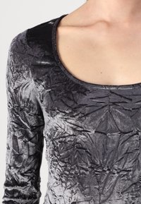 Maglietta a maniche lunghe in velluto nero stropicciato, con scollatura a barchetta e un intricato motivo a foglia lungo tutta la stoffa.