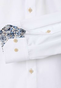Witte button-up shirt met een gemêleerd blauwe en crèmekleurige manchet. Voorzien van beige knopen en een gladde textuur. De manchet toont een bloemontwerp.