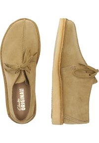 Beige suede kengät, joissa on pyöreä kärki, nauhakiinnitys ja vaaleanvärinen kuminen crepe-pohja. Ompeleet reunojen ympäri.