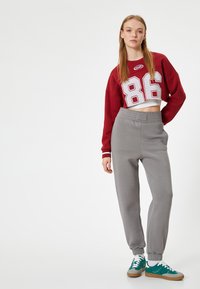 Rode cropped sweatshirt met witte mesh cijfers, gecombineerd met grijze tapered sweatpants en teal sneakers; casual sportieve outfit.