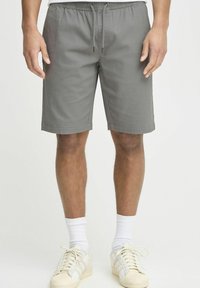 Gray cotton shorts with an elastic waistband and drawstring, featuring side pockets and a straight cut, shown with white sneakers and socks.