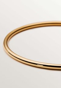 Brazalete de metal color dorado con forma redonda y suave. Presenta un acabado brillante y un grosor uniforme en toda su circunferencia.