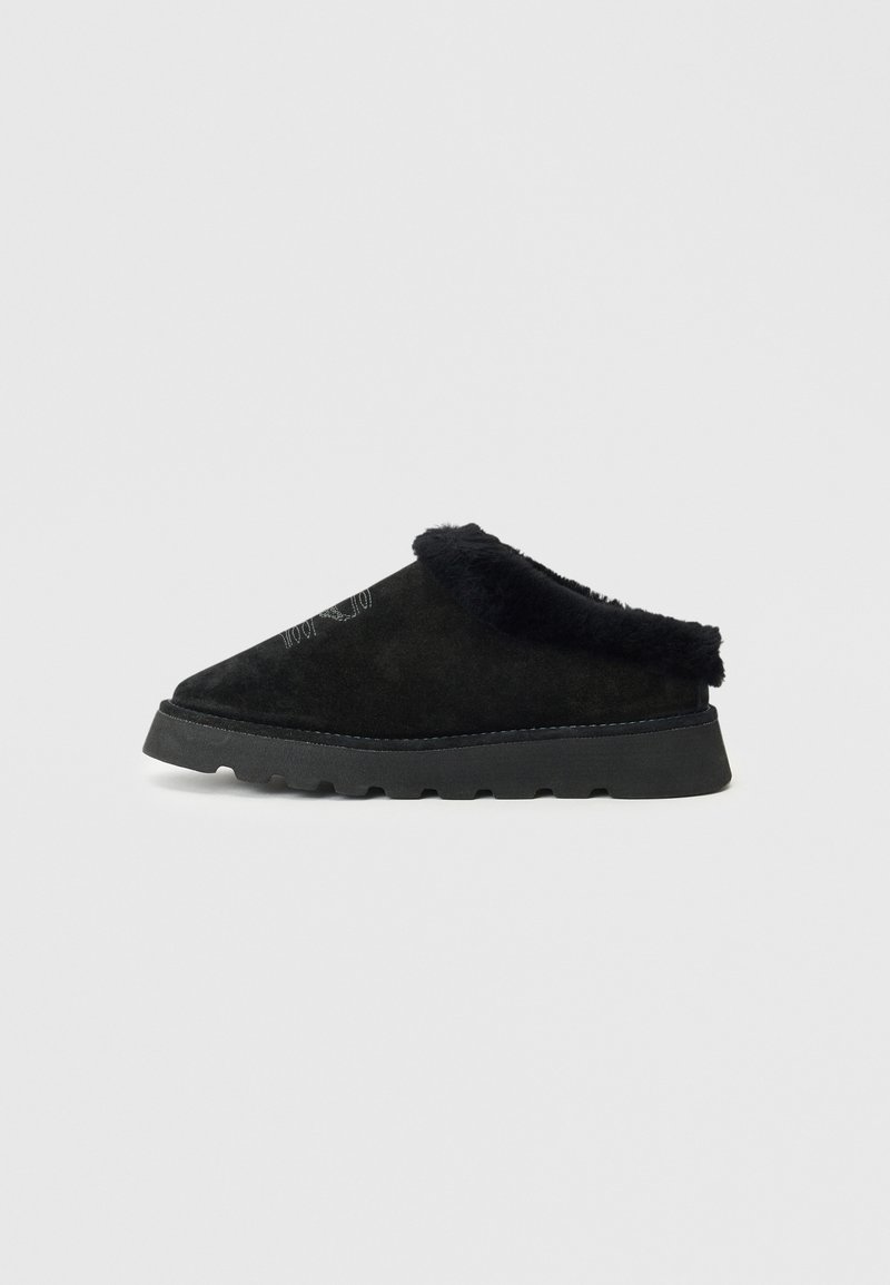 Sapato preto de slip-on feito de camurça com uma borda preta felpuda. Apresenta uma sola grossa e texturizada com ranhuras para aderência e um design de bico pontudo.