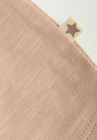 Gros plan d’un coin de tissu tricoté rose clair avec une petite étiquette beige ornée d’une étoile marron sur fond blanc.