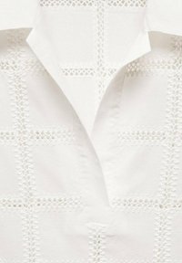 Witte katoenen shirt met een uitgesneden kantpatroon in een ruitdesign, met een notch-kraag en textuurelementen.