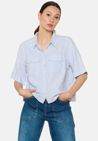 Camicia a righe azzurro chiaro con maniche corte, due tasche sul petto e chiusura con bottoni. Abbinata a jeans blu slim fit.