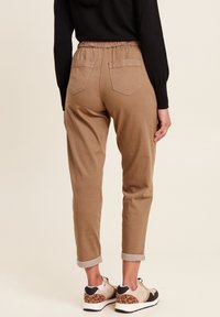 Tan broek met een elastische tailleband, twee achterzakken en opgerolde manchetten. Draagt met beige en zwarte sneakers met een luipaardprint accent.