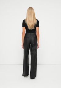 Pantaloni negri cu picioare largi, confecționați dintr-un material neted, având talie înaltă, buzunare la spate și un finisaj elegant. Modelul poartă un top negru ajustat.