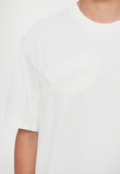 T-shirt bianca in cotone con collo rotondo e maniche corte, dotata di taschino sul petto e di un discreto marchio in rilievo sulla parte anteriore.