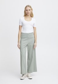 Body blanc à manches courtes associé à un pantalon à carreaux verts à taille haute et jambes larges. Le modèle porte des baskets blanches. Design simple et moderne.
