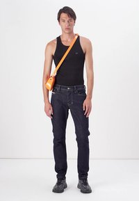 Čierny top na ramená, tmavé denimové džínsy a čierne topánky. Oranžová crossbody taška spočíva na pleci. Jednoduchý a neformálny outfit s jasnými líniami.