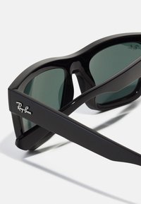 Ochelari de soare Ray-Ban negri au un cadru îndrăzneț și unghiular, cu lentile de culoare verde închis. Logo-ul este gravat pe bradă. Material din plastic fin.