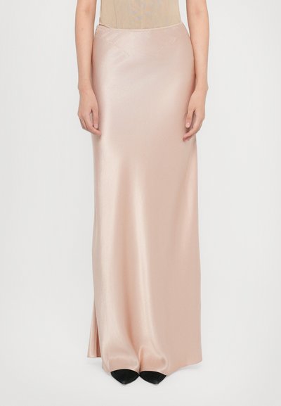 Satin-maxikleid in Blush-Pink mit glatter Textur, seitlichem Schlitz und leichtem Glanz, kombiniert mit schwarzen, spitzen Schuhen.