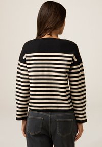 Pulover dungi negru și crem cu mâneci lungi, croială lejeră, și guler și manșete ribbate, asortat cu blugi închis la culoare.