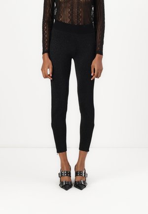 Black, glittery fitted leggings with a high waistband, tapered legs, and zipper accents at the hem. Paired with pointed black heels featuring straps.