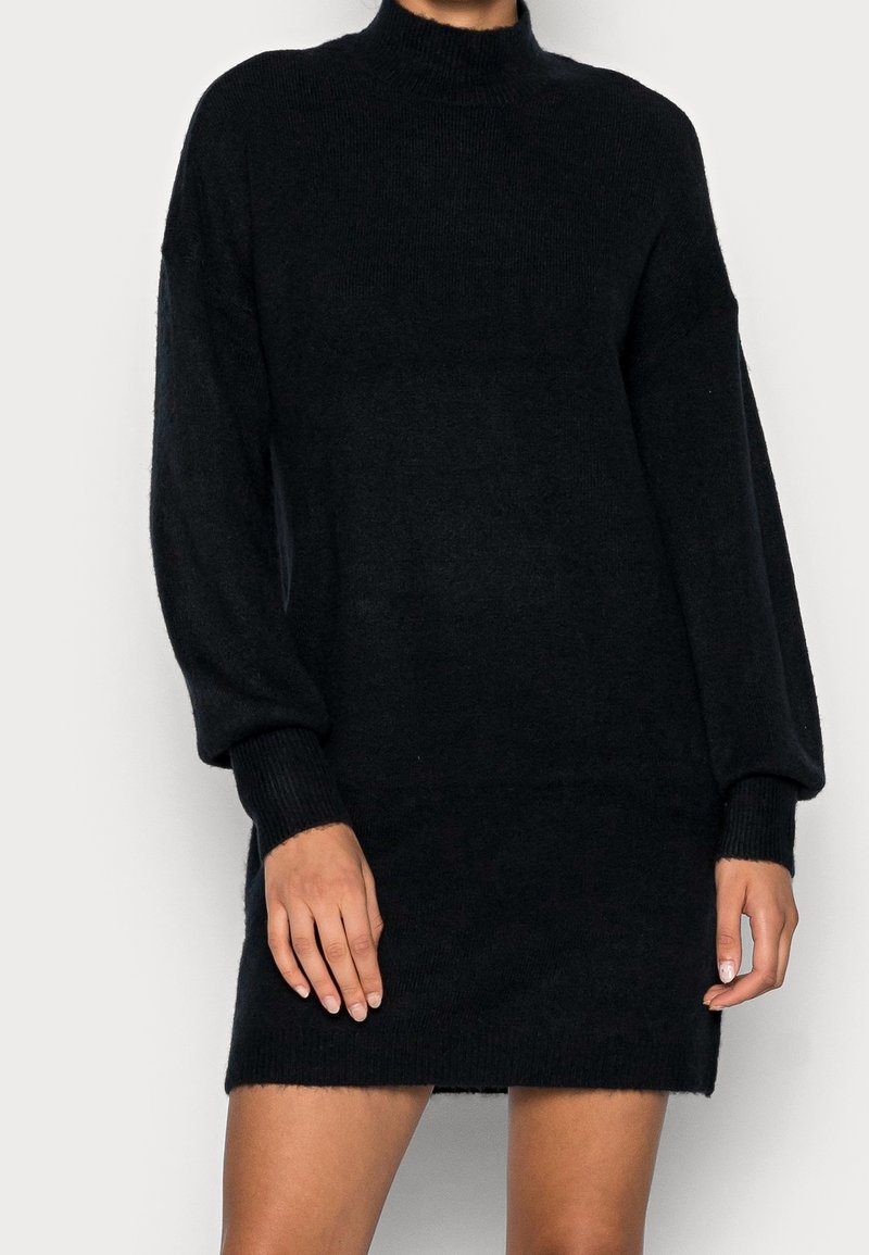Abito maglione nero a maglia con collo alto, maniche ampie e polsini a coste, caratterizzato da una morbida texture e una vestibilità rilassata.