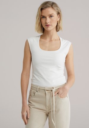 Fehér ujjatlan top négyzet alakú nyakkivágással, sima anyagból készült, világos bézs, magas derekú nadrággal párosítva, melyen húzózsinór található.