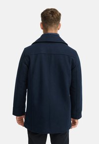 Marineblauer Wollmantel mit strukturierter Silhouette, Reverskragen und Rückenpasse. Ausgestattet mit langen Ärmeln und seitlichen Taschenöffnungen.
