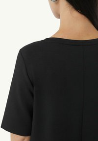 Haut noir à manches courtes avec un col rond et une texture lisse. Présente un détail de couture centrale à l'arrière.