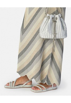 Pies con sandalias plateadas de tiras, falda a rayas beige y gris, y un bolso blanco con cordón y textura.