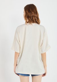 Oversized cream t-shirt with short sleeves, smooth texture, and a rounded neckline, paired with denim shorts. Simple, modern design.