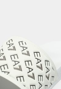 Άσπρο σανδάλι slide με φαρδιά λωρίδα που φέρει μαύρο εκτύπωμα λογότυπου EA7. Λεία υφή με διακριτικό μοτίβο, σχεδιασμένο για άνεση.