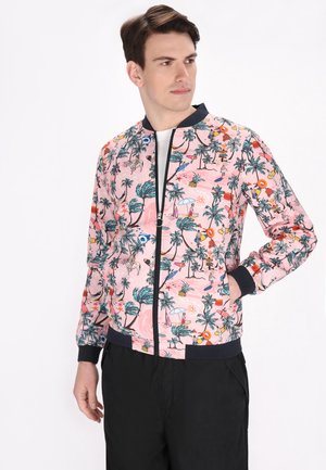 Roze bomberjack met een tropische print van palmbomen, zon en strandelementen. Zwarte geribbelde manchetten en tailleband met ritssluiting.