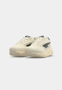 Beige athletic shoes with textured fabric and rubber soles, featuring a dark grey logo and accents, rounded toe, and lace-up design.