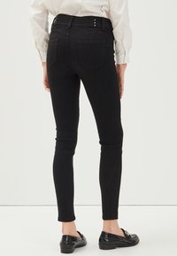 Jeans skinny neri con una vita alta, caratterizzati da bottoni decorativi e tasche posteriori. Il materiale è liscio ed elastico, offrendo un aspetto aderente.