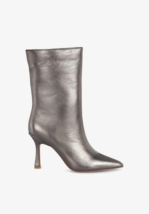Bottine argentée métallique avec un bout pointu, finition en cuir lisse et un talon haut élancé. Design épuré avec peu de couture visible.