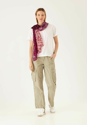 Weißes Baumwoll-T-Shirt, beigen Cargo-Hosen und einen rosa, sternmusternden Schal. Der Schal hat ein Farbverlauf-Design und wird über die Schulter gelegt getragen.