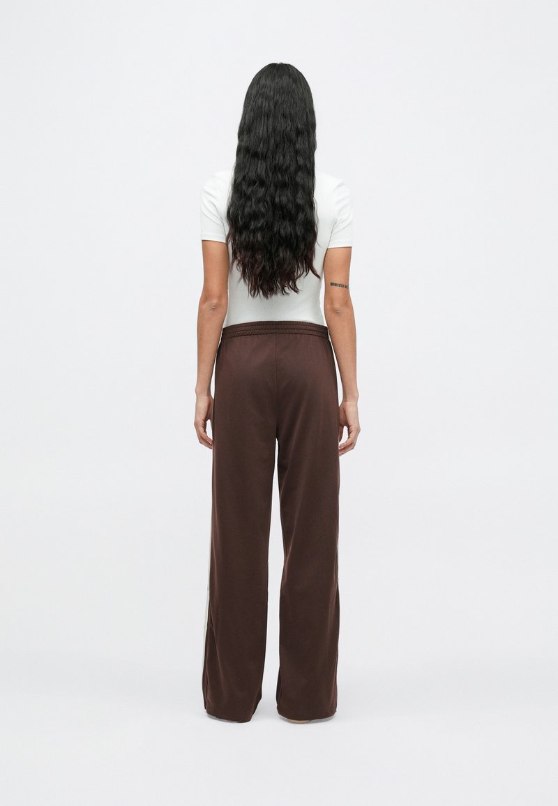 Pantalones anchos marrones con cintura elástica, combinados con una camiseta blanca ajustada de manga corta, vistos desde atrás con cabello largo y oscuro.