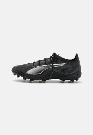 Botines de fútbol negros con un upper texturizado, acentos plateados y cordones prominentes. Presenta una suela resistente con múltiples tachones para tracción.